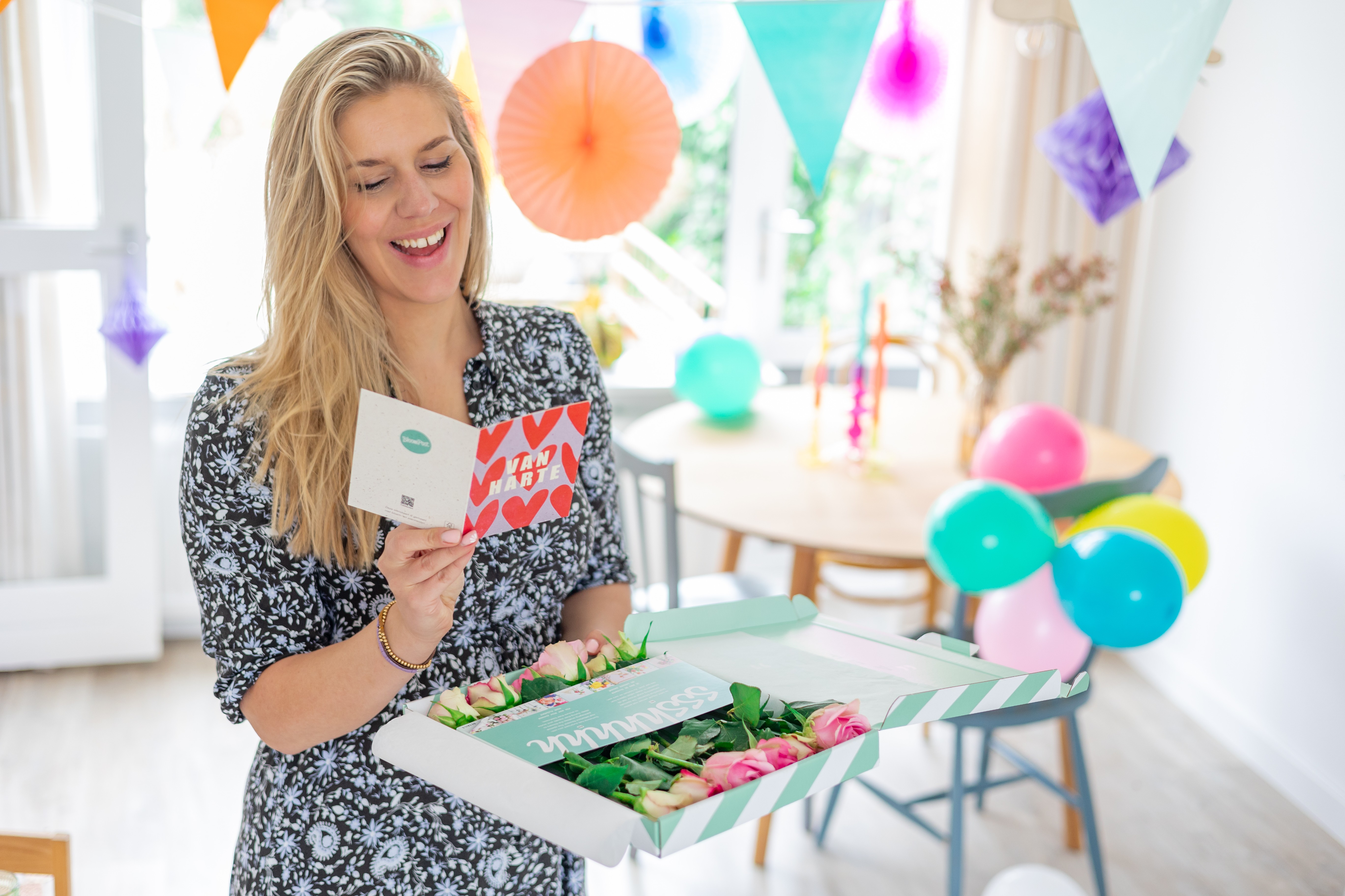 vrouw leest lachend een verjaardagskaart met brievenbus cadeau met rozen in handen