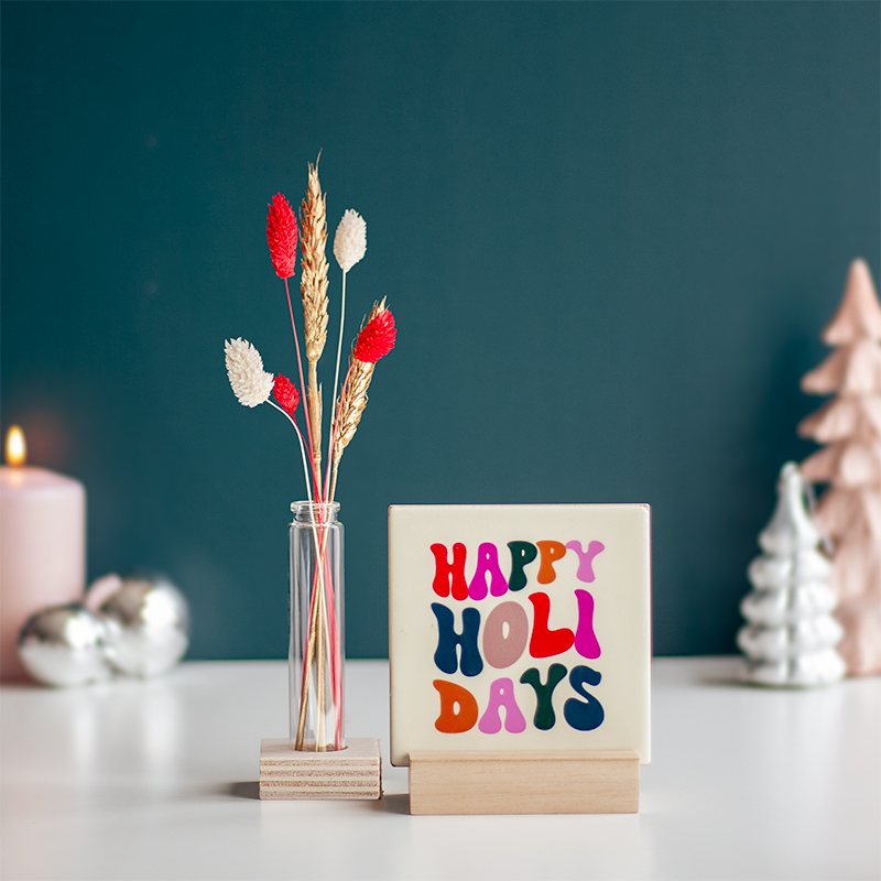 Kersttegeltje met tekst happy holidays in retro stijl en vaasje droogbloemen ernaast
