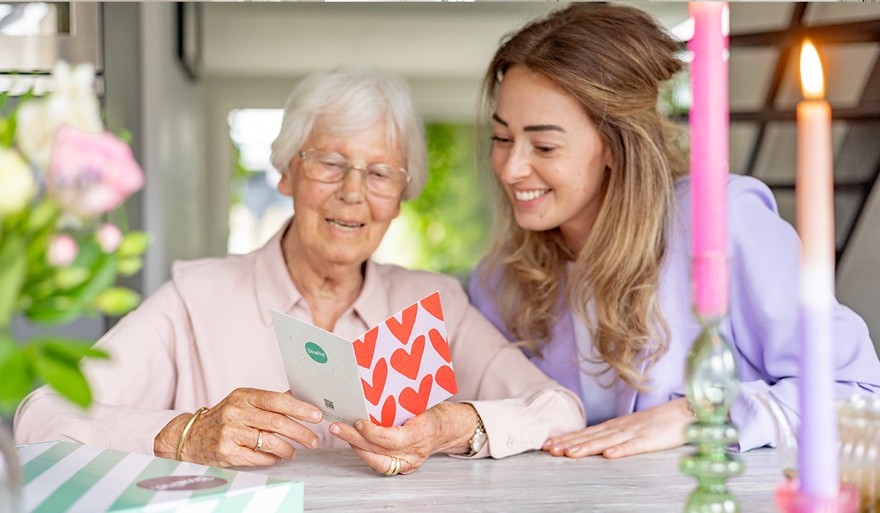 Oma leest wenskaart met hartjes erop, kleindochter zit er lachend naast