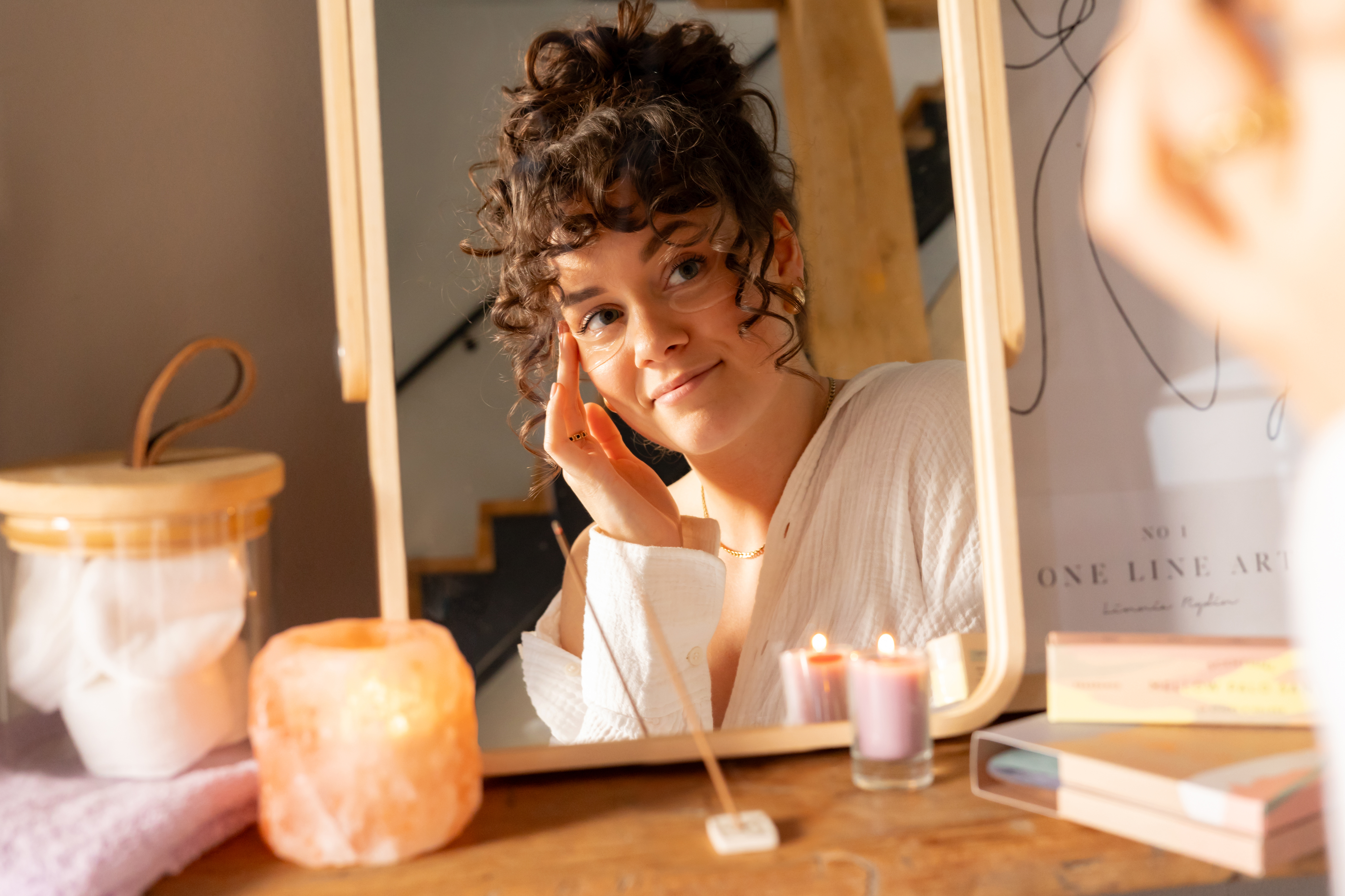 vrouw kijkt glimlachend in spiegel met kaarsje en wierook voor zich
