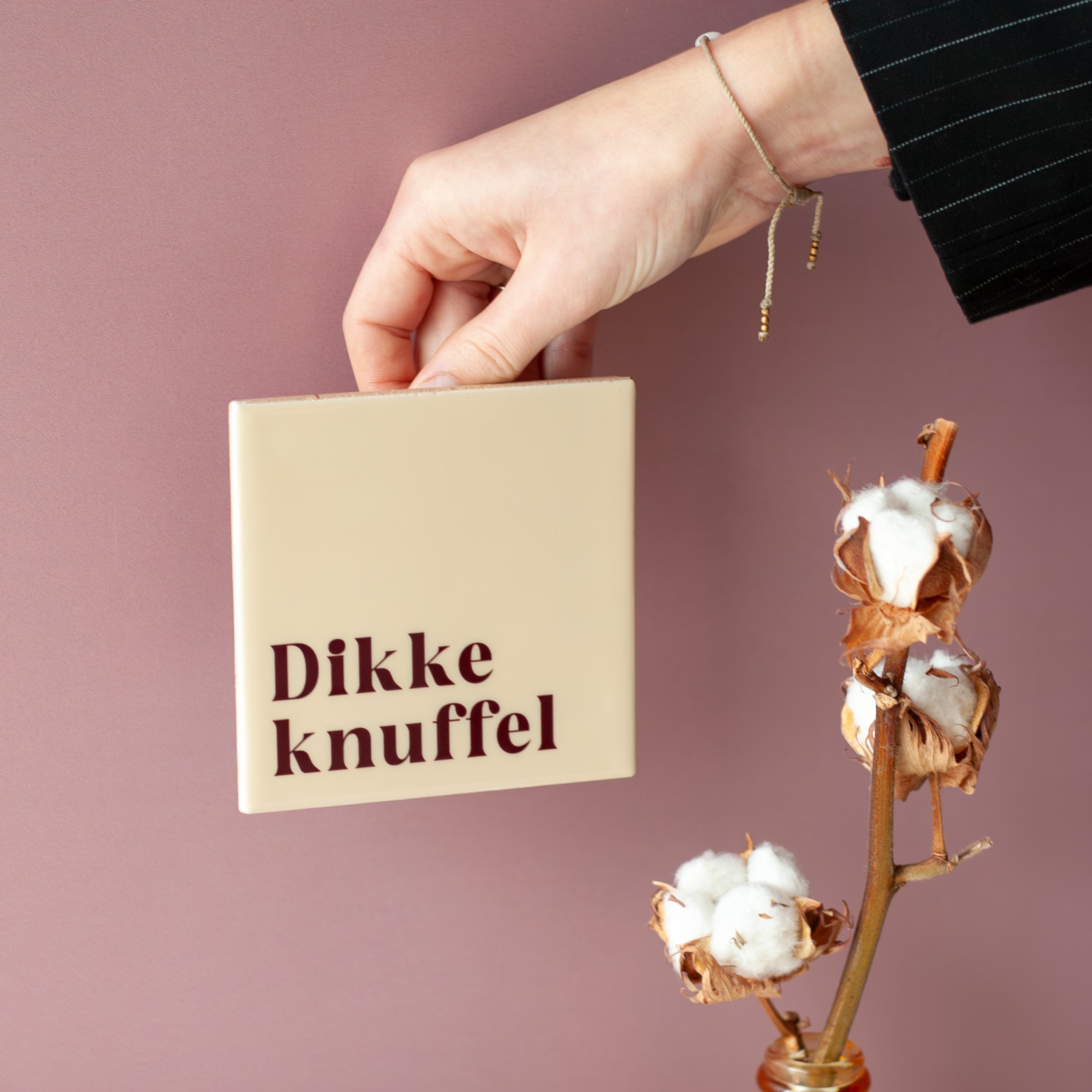 Tegeltje met tekst 'Dikke knuffel' wordt voor een muur vastgehouden 